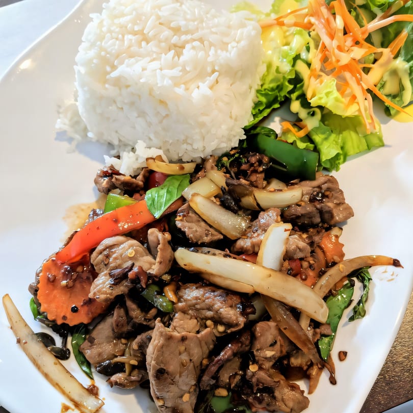 Bangkok Corner's Thai stir-fry with meat, vegetables, rice, and a side salad on a white plate.