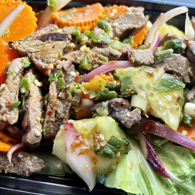 Close-up of a Thai beef salad with sliced meat, carrots, onions, and green vegetables.