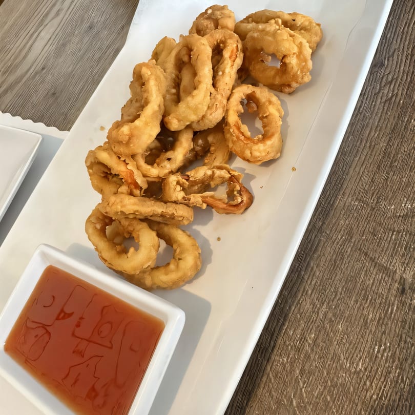 Crispy fried calamari rings with a side of sweet chili dipping sauce on a white plate.