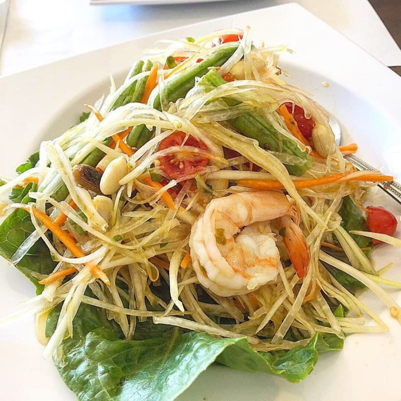 A vibrant Thai papaya salad with shrimp, green beans, tomatoes, and peanuts on a white plate.